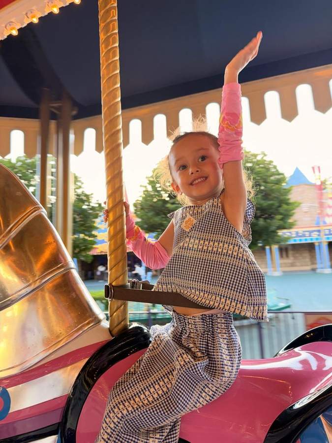 Leonie smiling and waving from a carousel horse