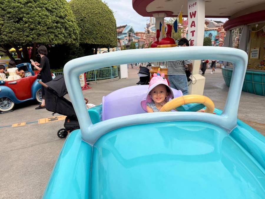 Leonie in a pink unicorn hat driving a turquoise toy car
