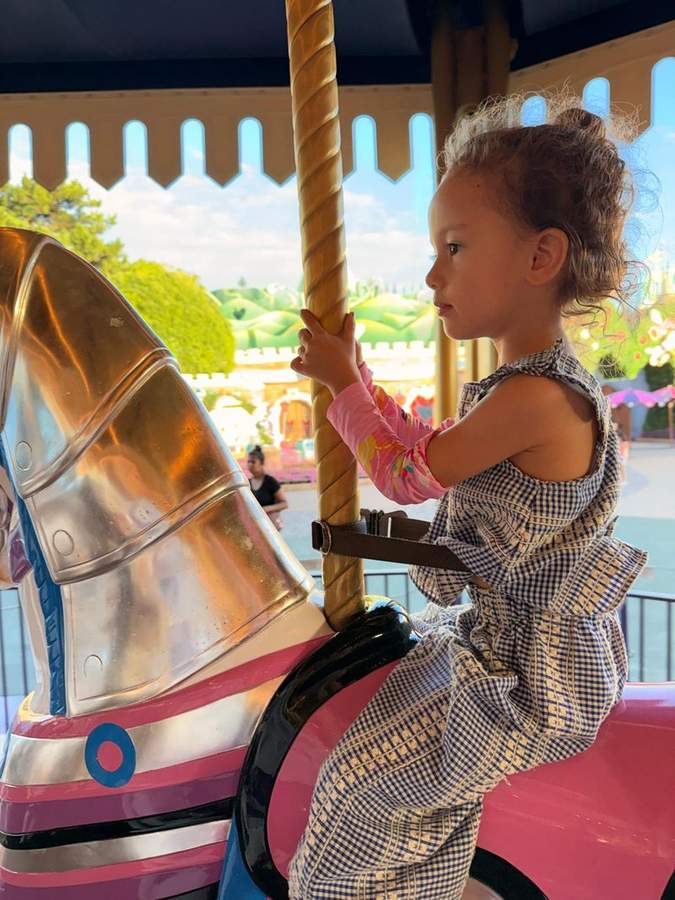 Leonie holding onto her carousel horse, looking out at the park